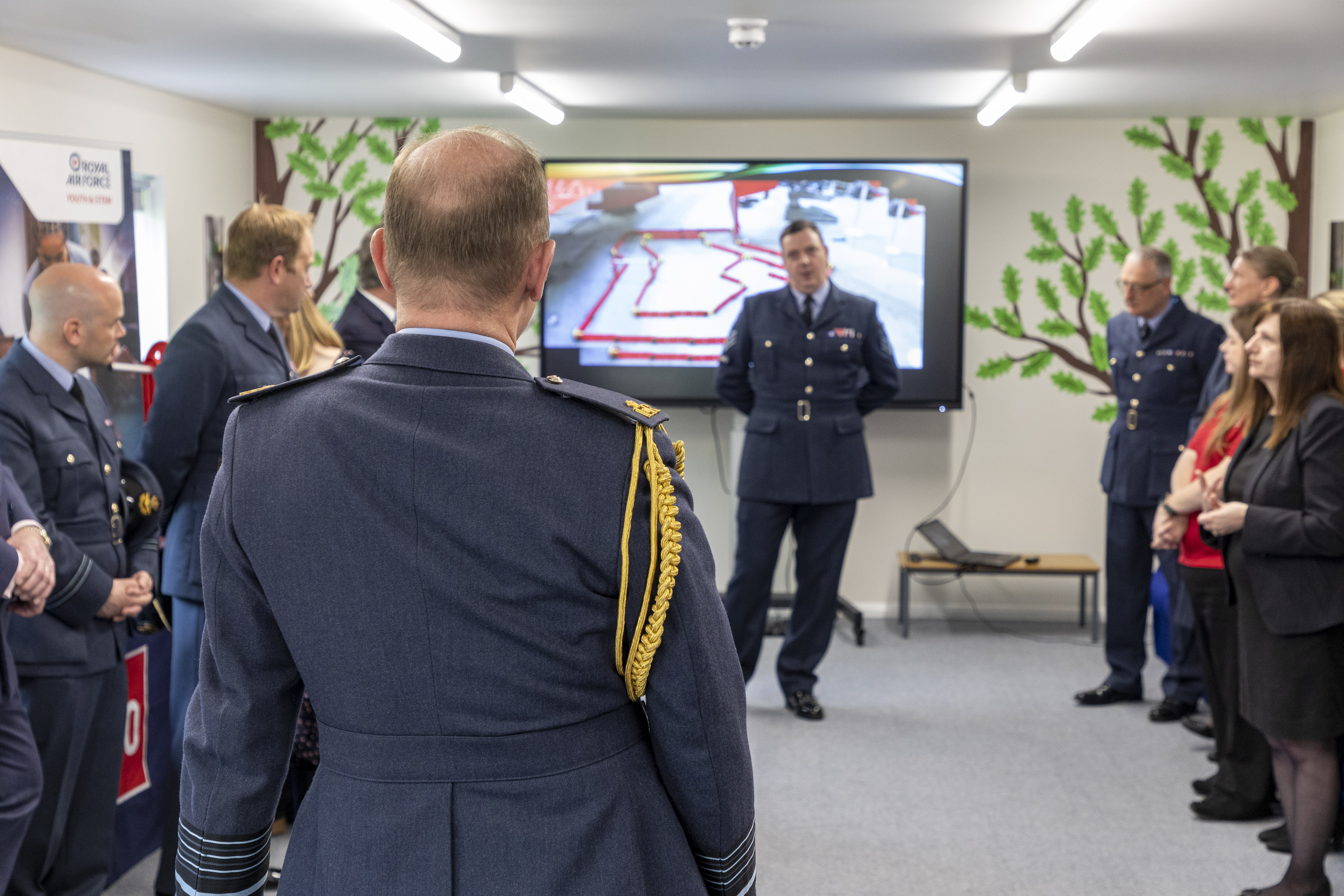 Aviators stand watching presentation with tv display.